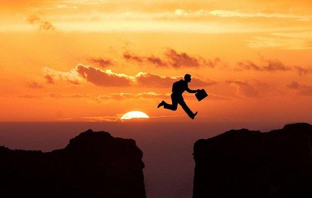 Businessman jumping a crevasse at sunset
