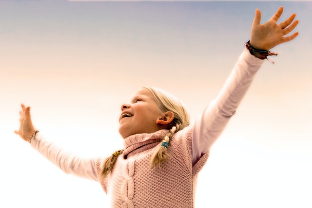 Young girl raises her arms to the sun