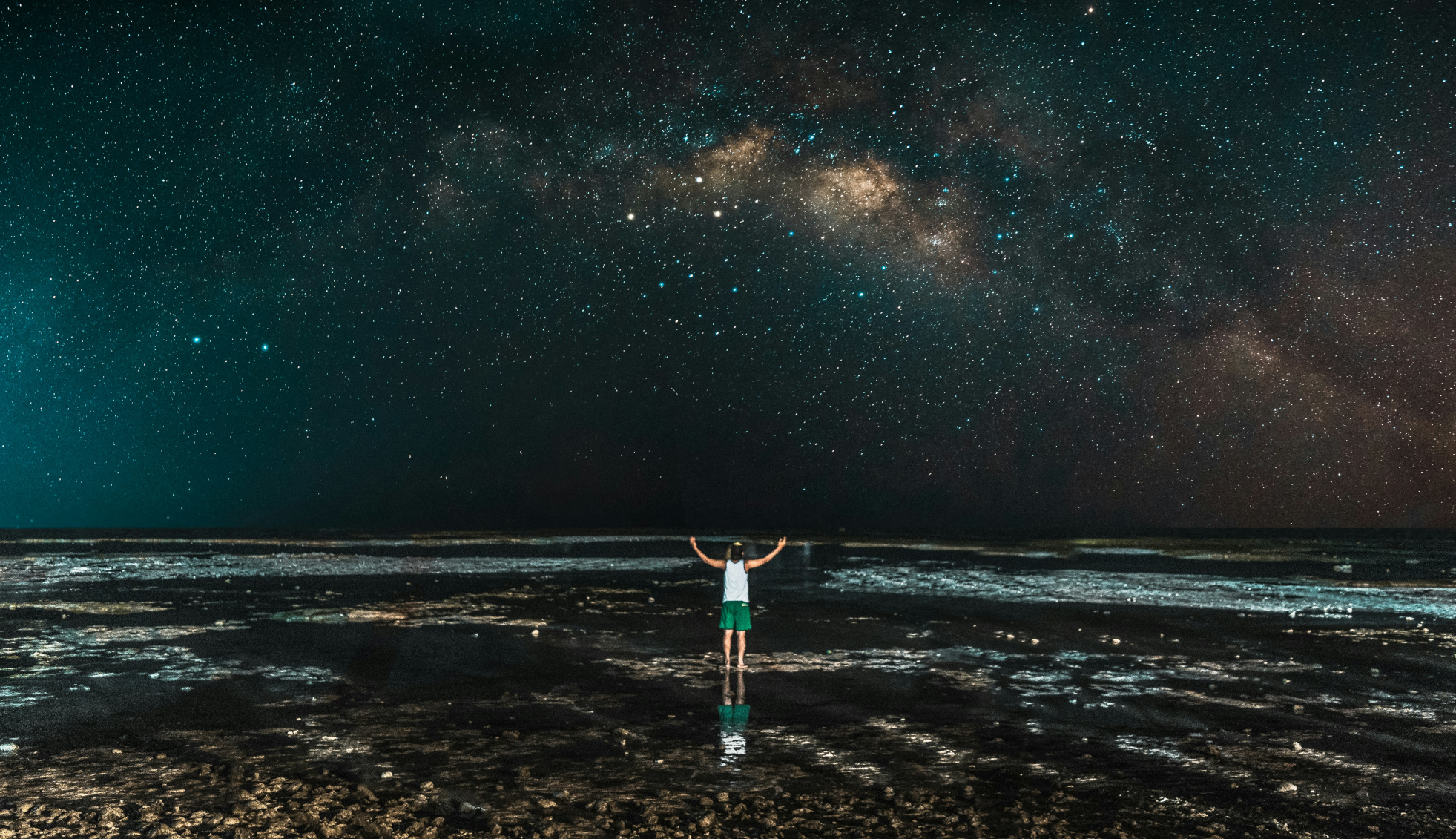 202609_universe_personsilhouettebeach_scale A person stands on the beach at night, in front of a field of stars in the night sky.